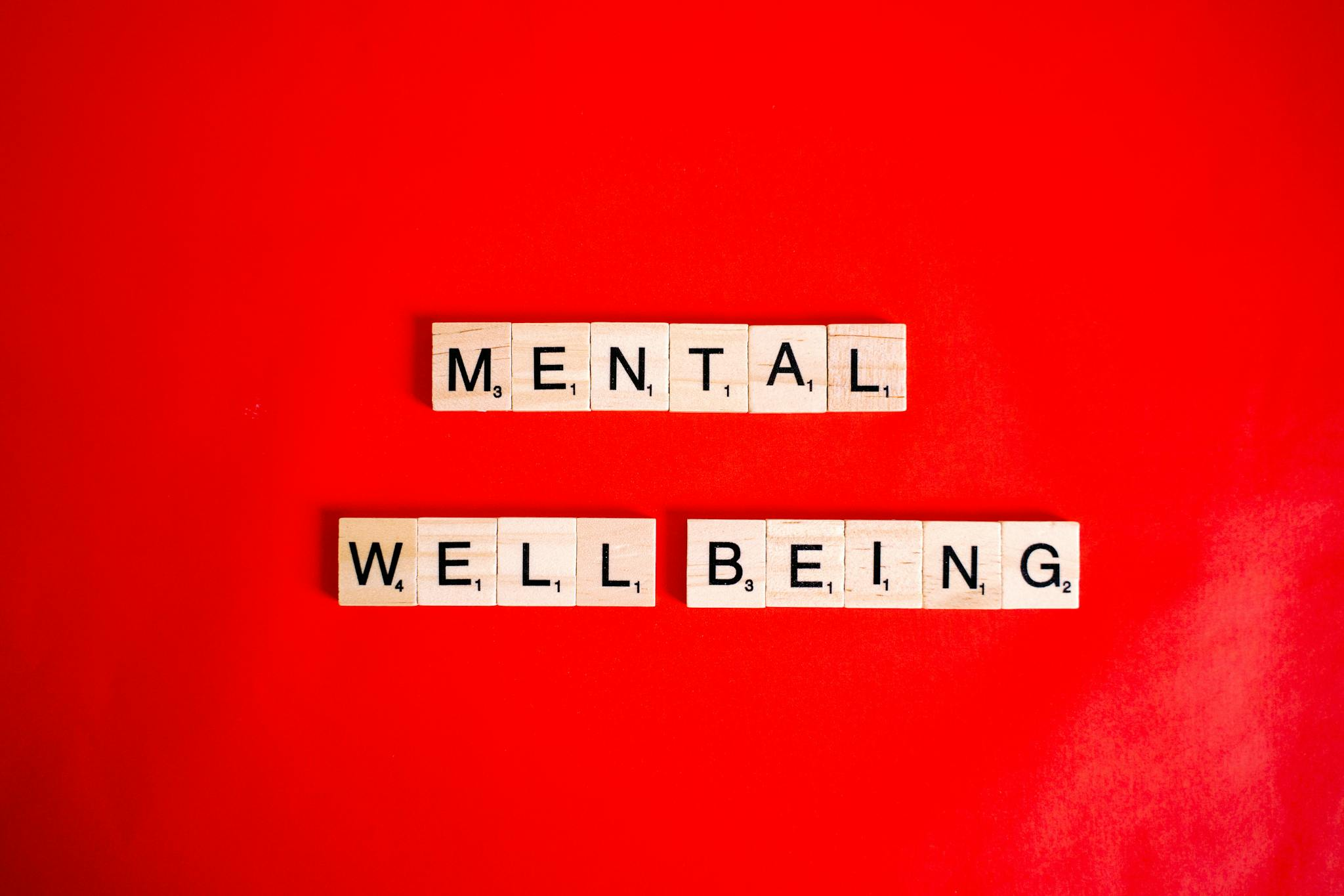 Wooden Scrabble tiles spelling 'mental wellbeing' on a vibrant red background.